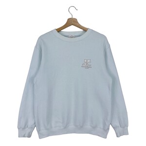 Puede incluir: Una sudadera de color azul claro con cuello redondo blanco y un peque&ntilde;o logotipo bordado en la parte delantera que dice "Courr&egrave;ges Paris".