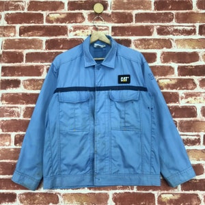 May include: A light blue work jacket with a black stripe and a yellow CAT logo on the chest. The jacket has multiple pockets and a button closure.