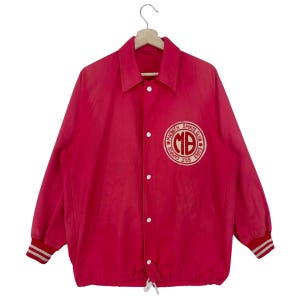 Könnte beinhalten: Eine rosafarbene Vintage-Baseballjacke mit einem weißen und roten gestickten Logo, auf dem "Macbeth Sports Club" und "Est. 1969" steht.