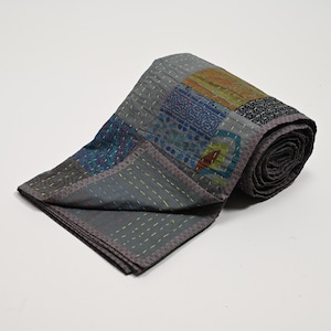 May include: A gray kantha quilt with a patchwork design featuring various colors and patterns. The quilt is rolled up and has a subtle sheen.