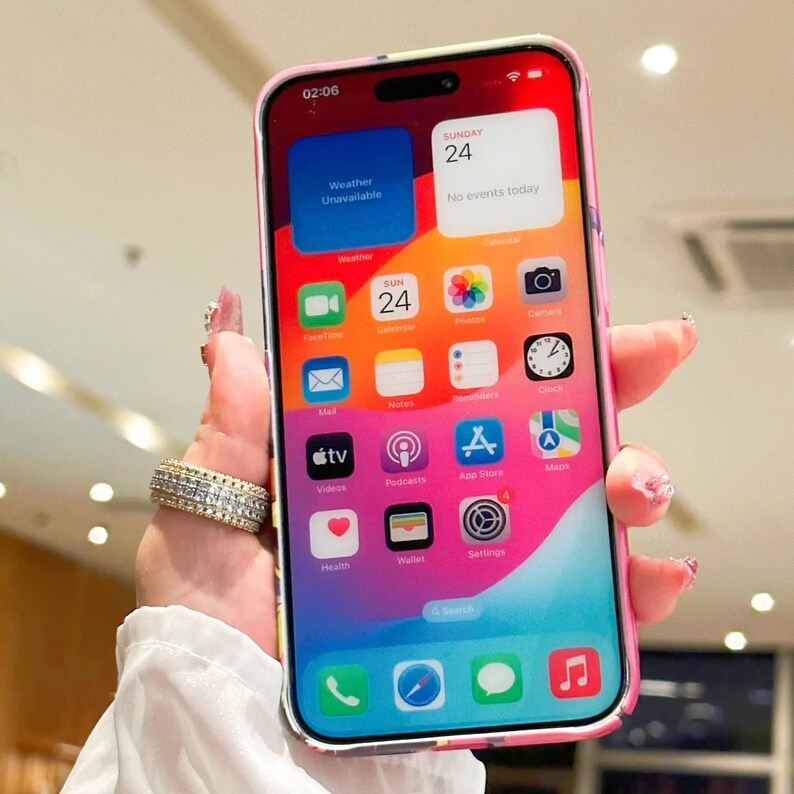 May include: A pink and white floral phone case with a clear back. The phone screen shows the time 02:06, the date Sunday 24, and several app icons. The text "Weather Unavailable" and "No events today" are visible on the screen.