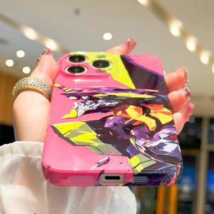 May include: A pink phone case with a colorful anime-style graphic of a robot. The case has a cutout for the phone's camera lens.