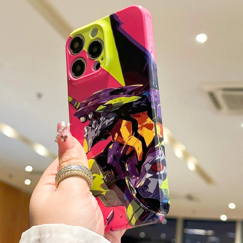 May include: A pink, black, and yellow phone case with a graphic of a purple and yellow robot with red eyes.