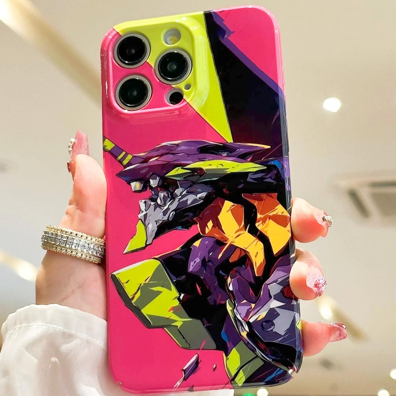 May include: A pink phone case with a green, yellow, and purple anime character design. The character has a large head and is facing the left side of the image. The phone case has a cutout for the camera lens.