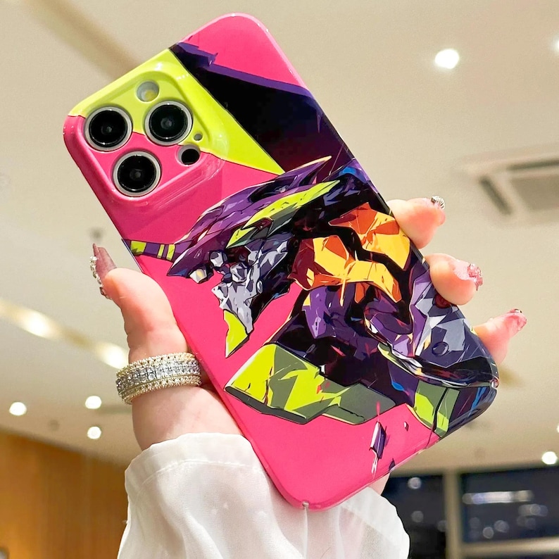 May include: A pink phone case with a graphic of a robot from the anime Neon Genesis Evangelion. The robot is in shades of purple, yellow, and green. The phone case has a cutout for the camera lens.