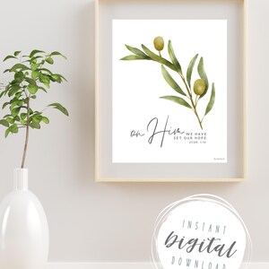 May include: A watercolor painting of an olive branch with the text "on Him we have set our hope 2 Cor. 1:10". The painting is framed in a light wood frame and is hanging on a white wall.
