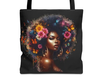 May include: Black tote bag featuring a vibrant illustration of a woman with a floral and butterfly-adorned afro. The artwork includes pink, yellow, and blue flowers, with orange and blue butterflies. The bag has black handles.