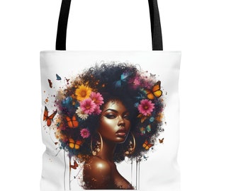 May include: A white tote bag with a black handle features a colorful illustration of a woman with an afro hairstyle adorned with flowers and butterflies. The woman has brown skin and is wearing large hoop earrings.