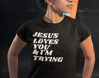 May include: Black t-shirt with white text that reads "JESUS LOVES YOU & I'M TRYING".