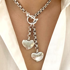 Puede incluir: Un collar de cadena de plata con cierre de palanca y dos colgantes de corazón.
