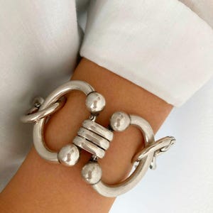 Peut inclure: Un bracelet en argent avec un grand design entrelacé et épais. Le bracelet a une finition polie et présente de multiples accents ronds.