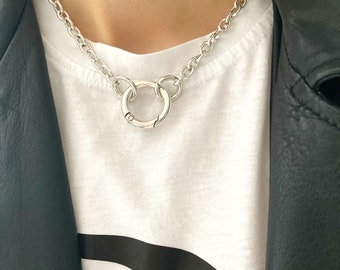 May include: A silver chain necklace with a large, round, silver pendant. The pendant is made of two interlocking circles.