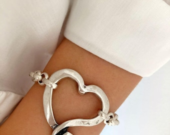 May include: A silver heart-shaped bracelet with a chain link design. The bracelet is open and has a textured finish.