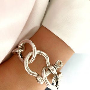 May include: A silver bracelet featuring a large, chunky, interlocking link design. The bracelet has a clasp that resembles a nautical shackle.