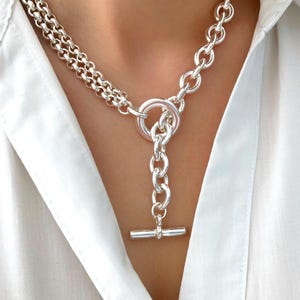 Könnte beinhalten: Eine silberne Kettenkette mit einem Toggle-Verschluss. Die Kette hat zwei verschiedene Kettenstile, eine ist eine zarte Kette und die andere ist eine dickere, massivere Kette.