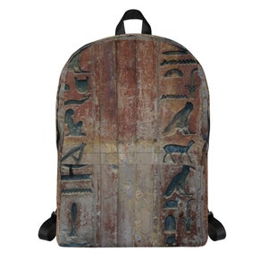 May include: A brown and beige backpack with an Egyptian hieroglyphic pattern. The backpack has black straps and a zipper closure.