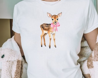 Pode incluir: Camiseta branca com um veado manchado de marrom e branco usando um laço rosa.
