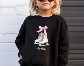 May include: Black sweatshirt featuring a graphic of ice skates with a pink bow and the name "Elizabeth" in white. The sweatshirt is worn by a child wearing sunglasses. The word "black" is printed in the lower right corner.