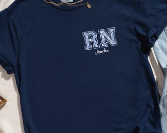 May include: A navy blue t-shirt with a white "RN" graphic and the name "Amelia" underneath. The shirt is made of a soft, comfortable material.
