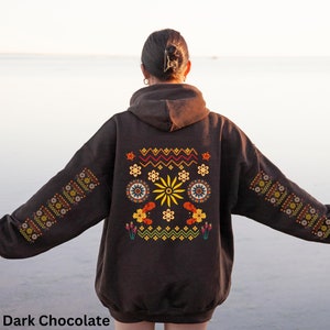 May include: A dark chocolate brown hoodie with a colourful embroidered design on the back. The design features geometric shapes, flowers, and a sun.