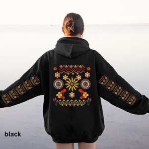 May include: Black hooded sweatshirt with a colourful embroidered design on the back. The design features geometric shapes, flowers, and a sun-like symbol.