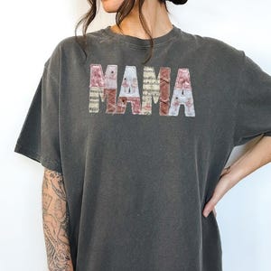 May include: Dark grey Comfort Colors 1717 Pepper t-shirt featuring the word "MAMA" in a floral and patterned design. The shirt has short sleeves and a relaxed fit, suitable for everyday wear.