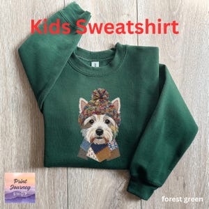 May include: A forest green kids' sweatshirt featuring an embroidered dog wearing a knitted hat and scarf. The text "Kids Sweatshirt" is in red. The sweatshirt is made of a soft material. The words "forest green" are at the bottom.