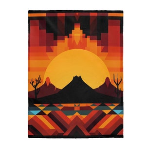 May include: Geometric pattern blanket with a sunset scene featuring a large orange sun, a mountain range, and two cacti. The blanket has a red, orange, yellow, and blue color scheme.
