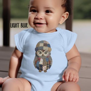 May include: Light blue baby onesie with a graphic of an owl wearing a patchwork hat and scarf. The text "LIGHT BLUE" is printed in black on the upper left side of the onesie. The baby is smiling.