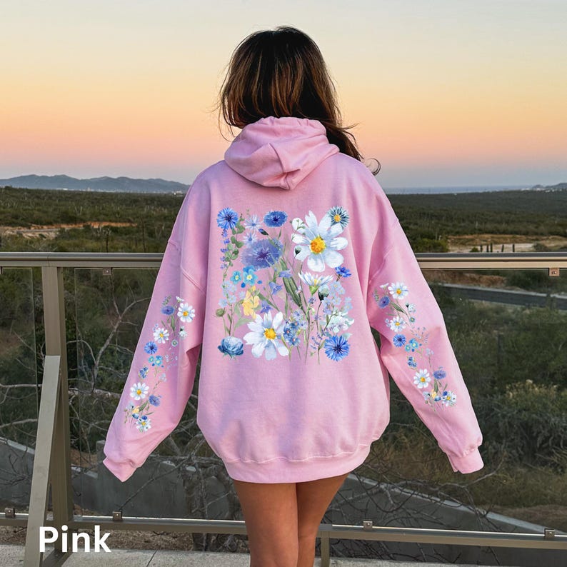 May include: A light pink hoodie with a floral design. The back of the hoodie features a large arrangement of white and blue flowers. Smaller floral patterns adorn the sleeves. The word "Pink" is at the bottom left.