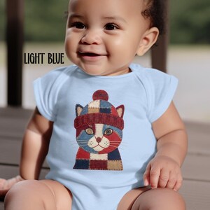 May include: Light blue baby bodysuit with a colorful patchwork cat design wearing a matching hat. The text "LIGHT BLUE" is printed on the top left of the bodysuit. The baby is smiling.
