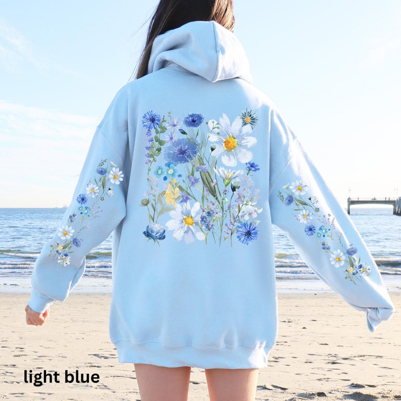 May include: Light blue hoodie with a floral design. The back features a square arrangement of blue, white, and yellow flowers. The sleeves have a smaller floral pattern. The text "light blue" is at the bottom.