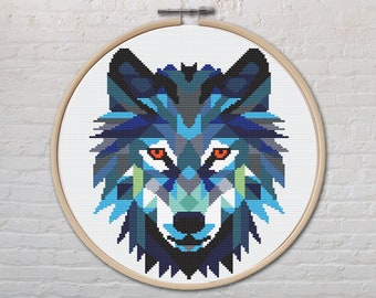 Peut inclure: Une broderie au point de croix d'un loup géométrique dans un cercle en bois. Le visage du loup est composé de formes bleues, turquoise, grises et noires avec des yeux orange. Le fond est blanc, et le cercle est en bois clair.