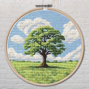 Op de afbeelding: Een borduurring met een kruissteekpatroon van een groene boom in een veld met een blauwe lucht en witte wolken.