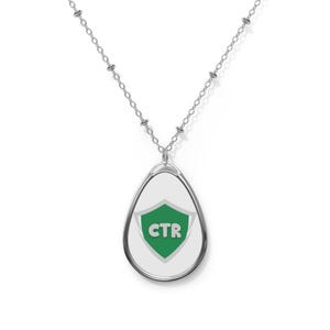 May include: A silver necklace with a teardrop-shaped pendant featuring a green shield with the letters "CTR" in white.