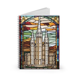 Puede incluir: Cuaderno con espiral con un diseño de vidriera que representa un edificio alto y blanco con agujas. La obra de arte incluye un cielo y un paisaje coloridos, con un borde negro y una encuadernación en espiral plateada. El cuaderno está abierto, revelando páginas rayadas.