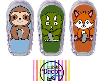 May include: Three colorful cartoon animal designs for a diabetic pump. The designs are a sloth, a dinosaur, and a fox. The designs are on a white background with a clear plastic overlay. The designs are for a product called "Diabetic Decor by Domica".