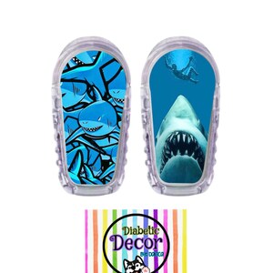 May include: Two clear plastic medical device covers with colorful shark designs. One cover features a close-up of a shark's mouth with sharp teeth. The other cover features a pattern of multiple sharks in blue and white. The covers are for a medical device and are sold by Diabetic Decor.