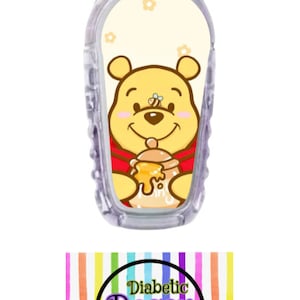 May include: A clear plastic medical device with a Winnie the Pooh themed sticker. The sticker features Winnie the Pooh holding a honey pot with a bee on his nose. The background is yellow with white flowers. The text "Diabetic Decor by: Damica" is on a rainbow striped background.