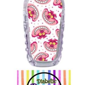 May include: A white and pink patterned medical device cover featuring the Cheshire Cat from Alice in Wonderland. The cover is designed to fit a continuous glucose monitor (CGM) and has a clear plastic backing. The text "Diabetic Decor by Donica" is visible in a circle with a rainbow background.