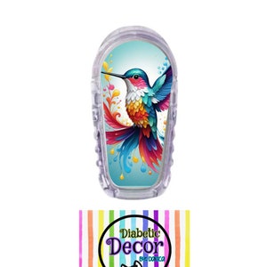 May include: A colorful hummingbird design on a clear plastic diabetic device cover. The cover has the text "Diabetic Decor by Domica" on a rainbow striped background.