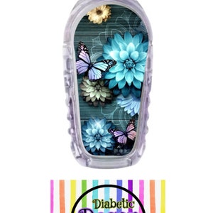 May include: A clear plastic medical device with a colorful sticker featuring a floral design with blue and purple butterflies. The sticker has a woodgrain background and the text "Diabetic Decor by: Danica".