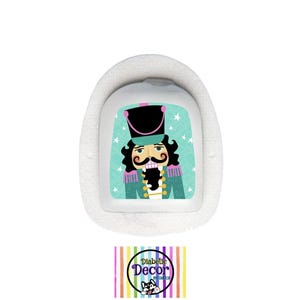 May include: A white medical device with a cartoon nutcracker soldier design. The nutcracker has a black hat, a large mustache, and a teal and pink uniform. The device has a white border and a logo at the bottom.