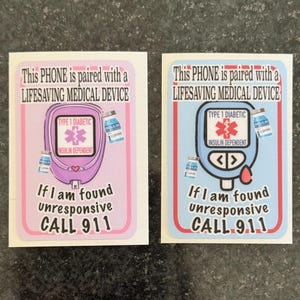 May include: Two stickers with text: "This PHONE is paired with a LIFESAVING MEDICAL DEVICE." One is pink, the other blue. Both have a graphic of a blood glucose meter with "TYPE 1 DIABETIC" and "INSULIN DEPENDENT." Text: "If I am found unresponsive CALL 999."
