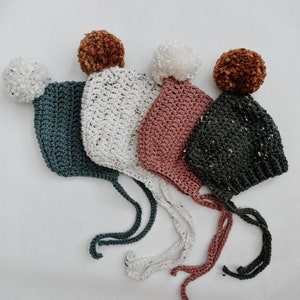 May include: Four crocheted baby hats with pom-poms in various colors, including teal, white, pink, and black.