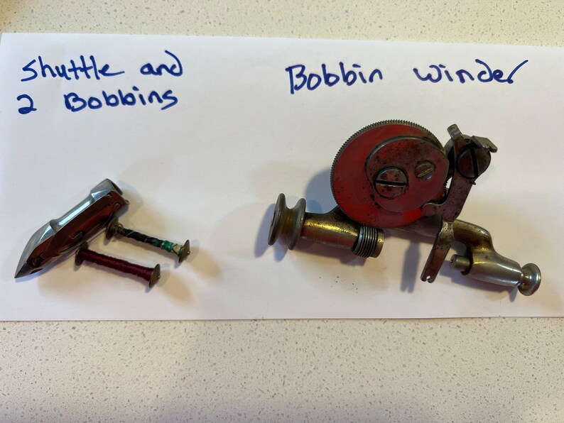 May include: A vintage sewing machine bobbin winder with a red metal spool and a silver metal base.  There is also a silver metal shuttle and two bobbins with thread.