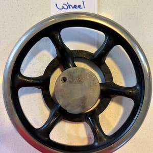 May include: A black metal hand wheel with six spokes and a silver rim. The wheel has a small hole in the center.
