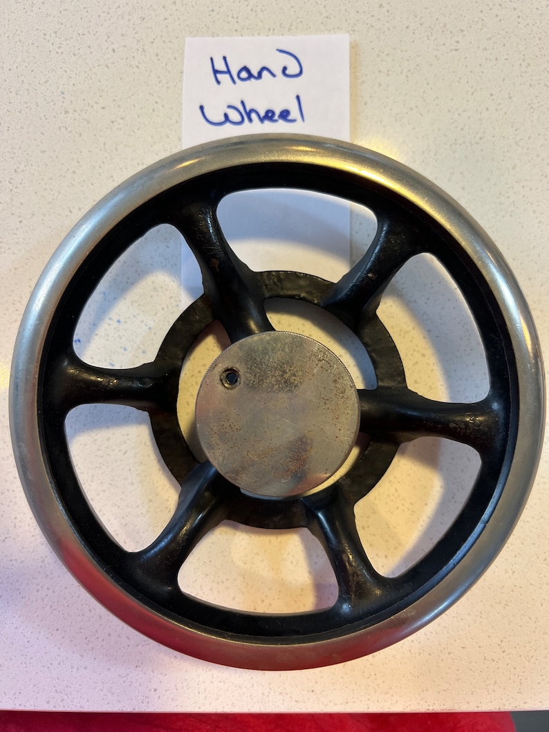 May include: A black metal hand wheel with six spokes and a silver rim. The wheel has a small hole in the center.