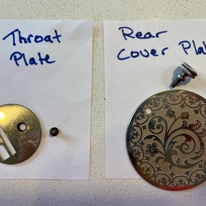 May include: Two sewing machine parts, a silver throat plate with a slot and a silver rear cover plate with a floral design. The rear cover plate has a small silver screw.