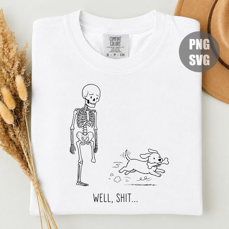 Puede incluir: Una camiseta blanca con un gr&aacute;fico de l&iacute;neas negras de un esqueleto al que le falta una pierna y un perro que sale corriendo con un hueso en la boca. Debajo de la ilustraci&oacute;n, el texto dice WELL, SHIT... La camiseta tiene una etiqueta Comfort Colors.